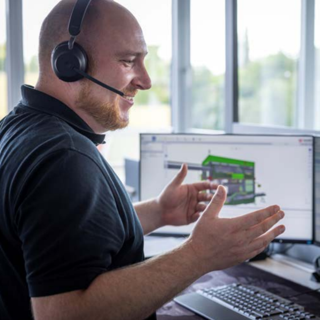 Technischer Experte, der über ein Headset Fernsupport für Kunden leistet und dabei mit einer digitalen Maschinenschnittstelle interagiert, die auf drei Monitoren angezeigt wird.