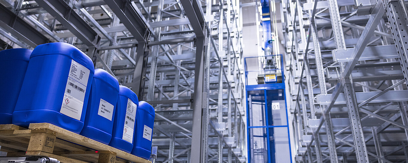 Photograph of Körber’s new automated high-rack warehouse with blue barrels on euro-pallets in the left corner.