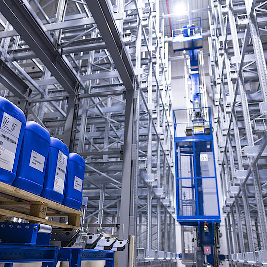 Photograph of Körber’s new automated high-rack warehouse with blue barrels on euro-pallets in the left corner.