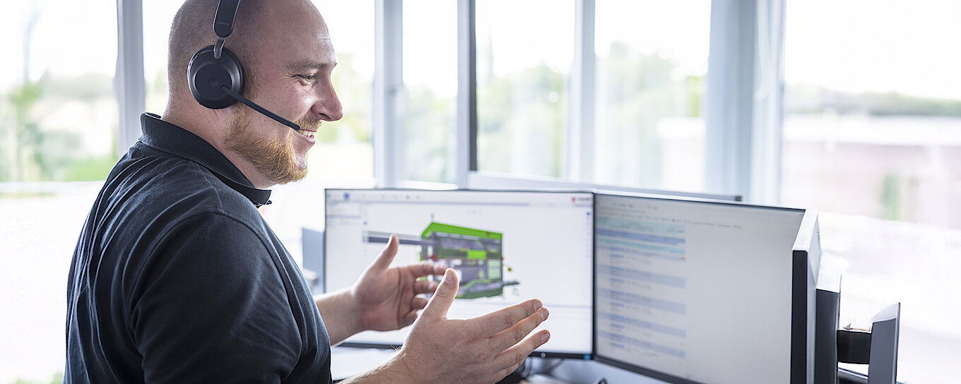 Technischer Experte, der über ein Headset Fernsupport für Kunden leistet und dabei mit einer digitalen Maschinenschnittstelle interagiert, die auf drei Monitoren angezeigt wird.